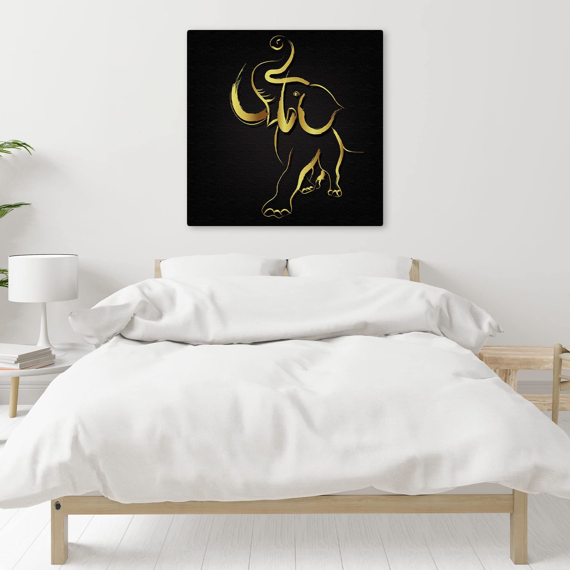 Abstract black and gold elephant art on canvas hanging above bed in minimalist bedroom with white linens and wooden furniture