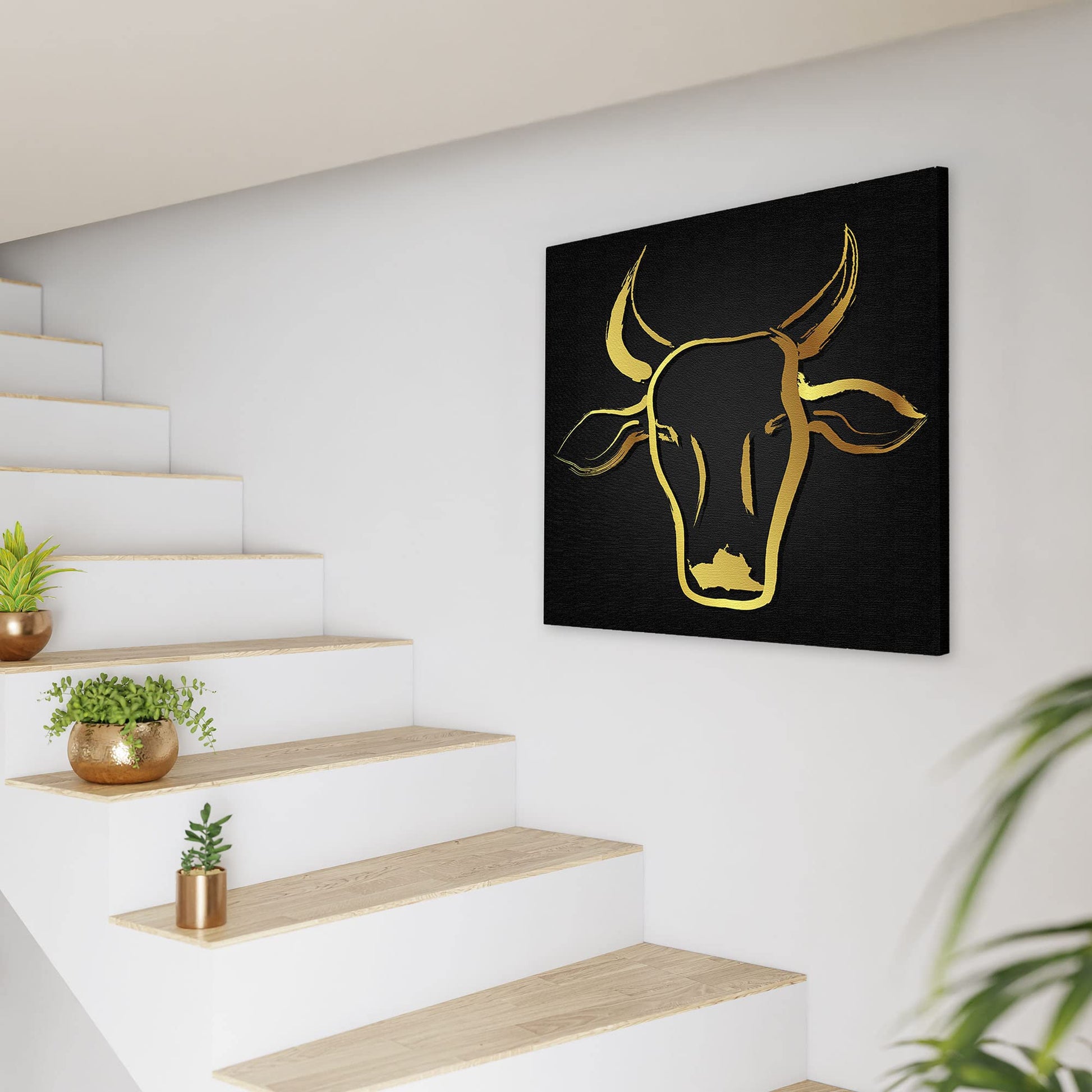 Black and gold abstract cow art with sleek brushstroke design on square canvas displayed on white wall near staircase