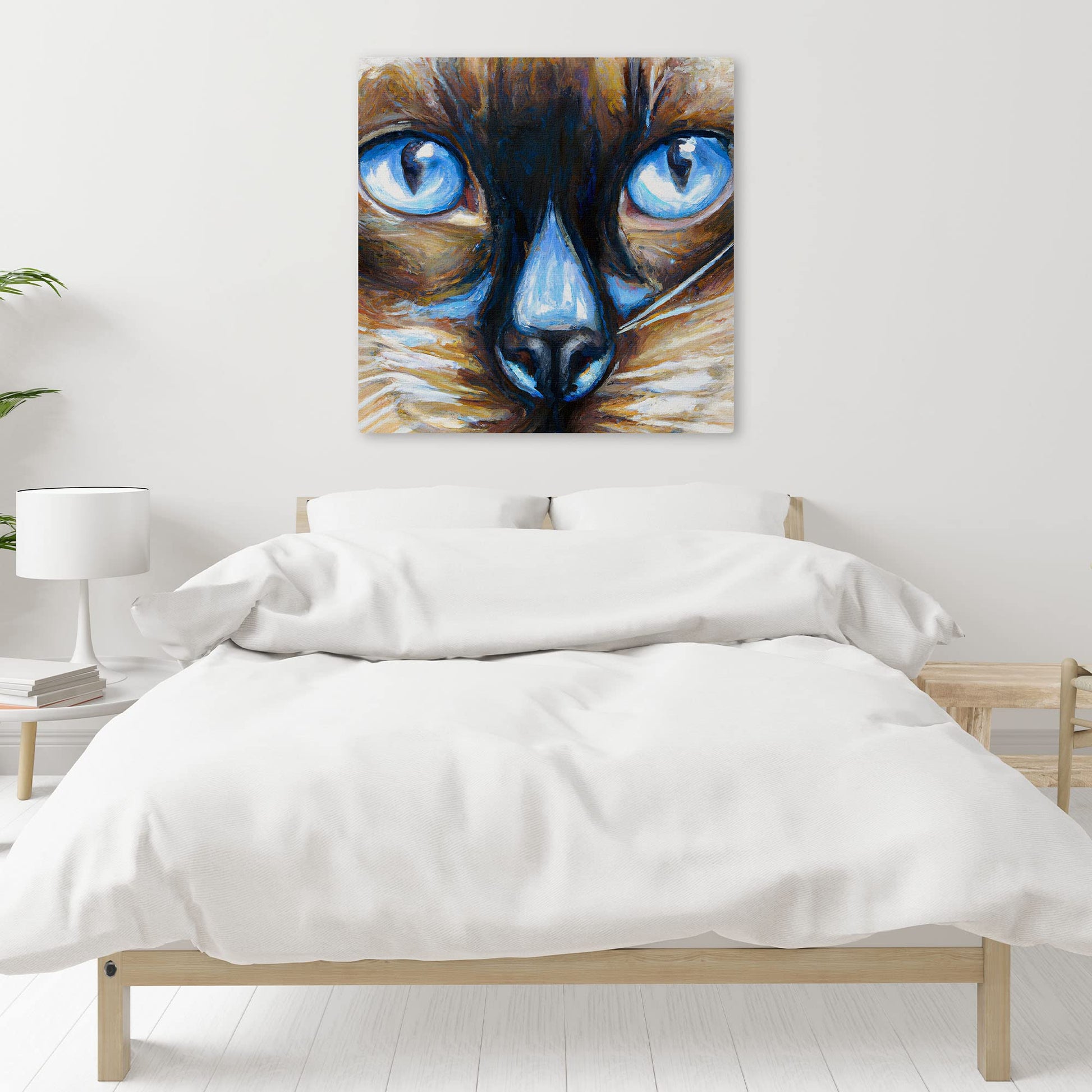 Close-up Siamese cat wall art with intense blue eyes and textured brush strokes on square canvas above white bed in minimalist room