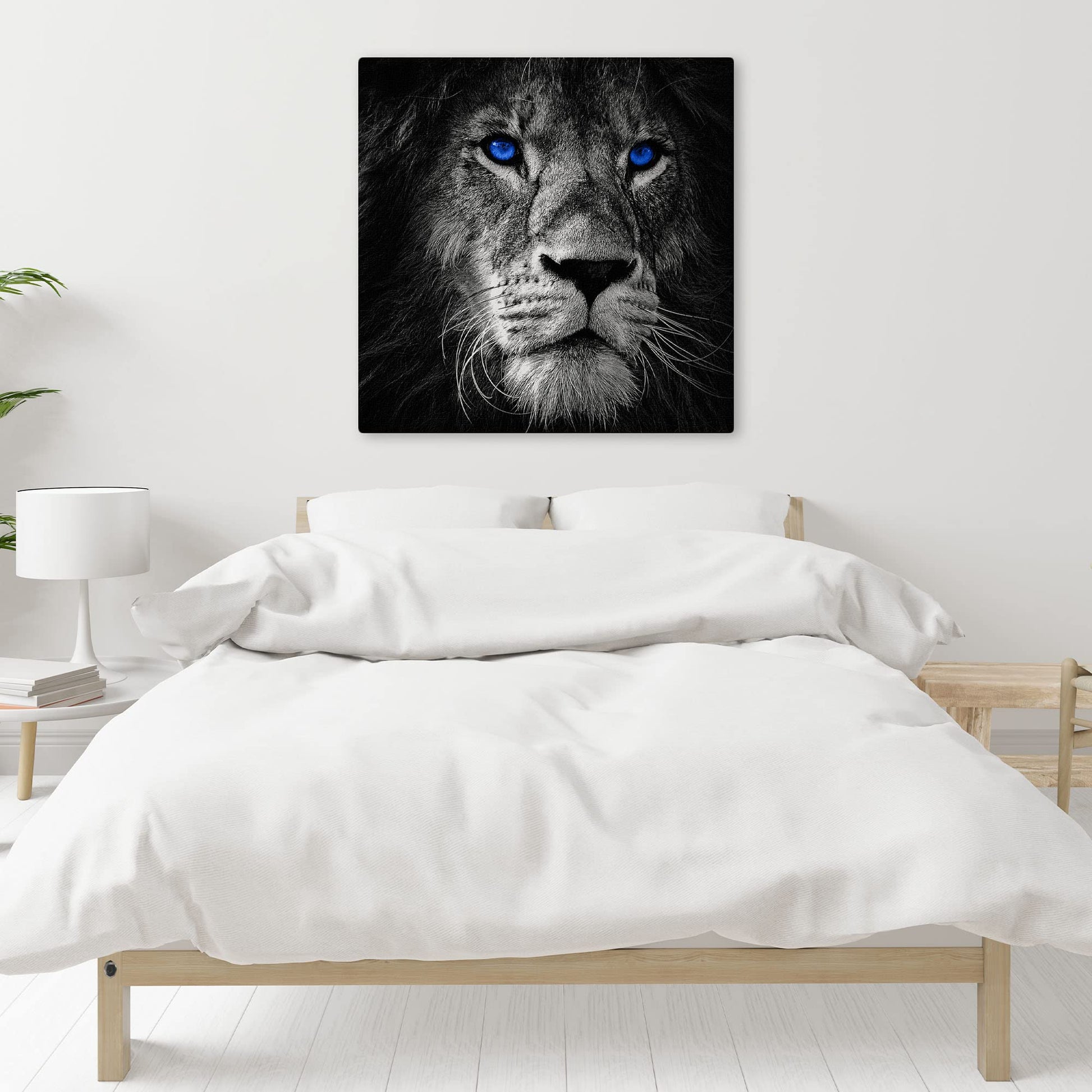 Black and white close-up lion face with bright blue eyes printed on canvas above minimalist wooden bed in white bedroom