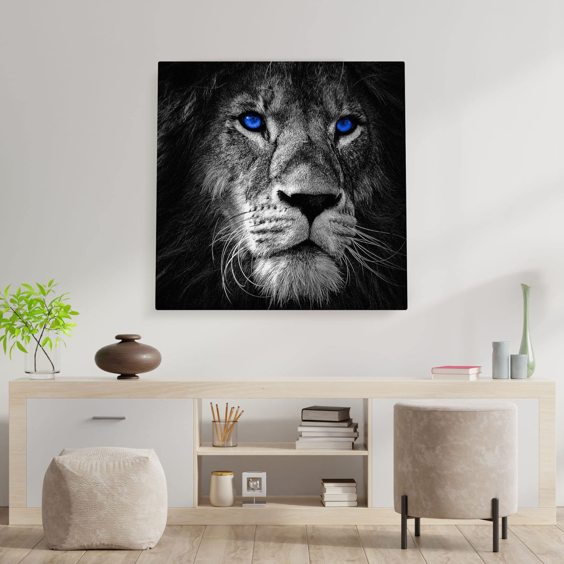 Black and white close-up lion face with vivid blue eyes printed on canvas hanging above minimalist wooden sideboard