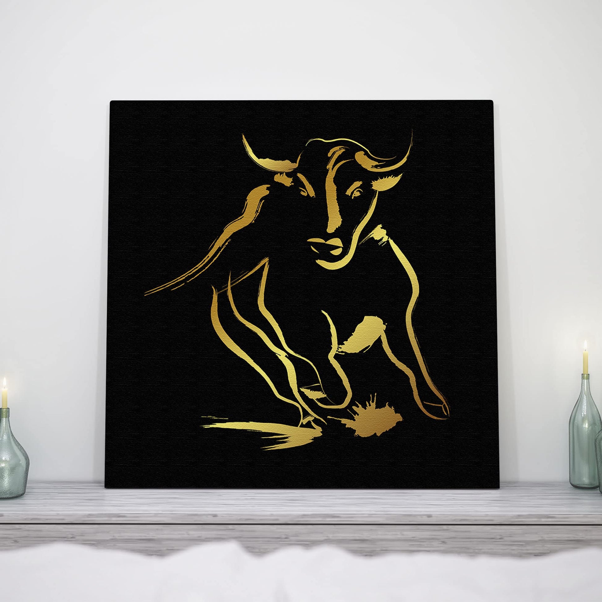Black and gold abstract bull art with fluid brushstroke design on square canvas displayed on white wall with decorative bottles