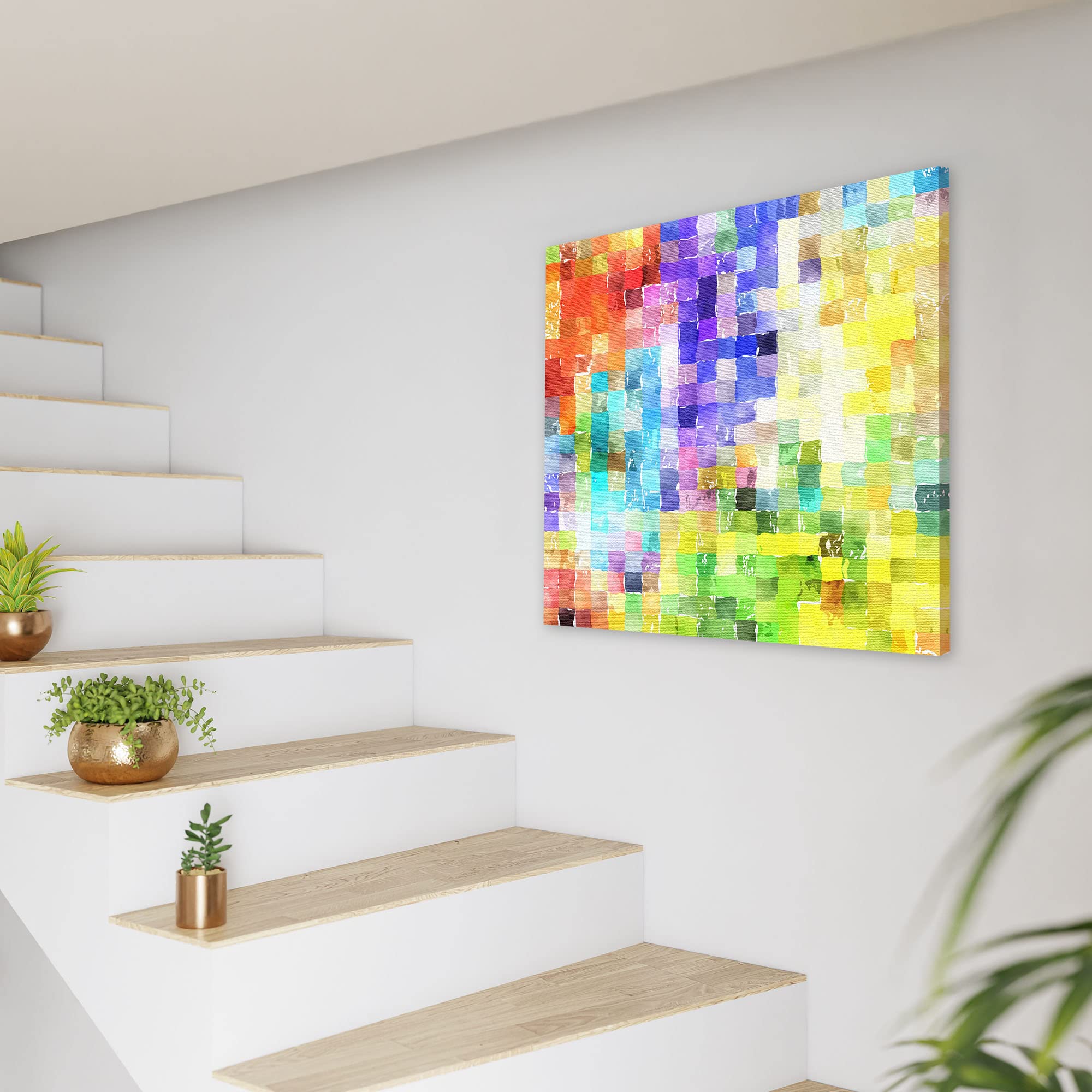 Colorful abstract watercolor mosaic wall art on square canvas displayed on white wall next to modern staircase with plants