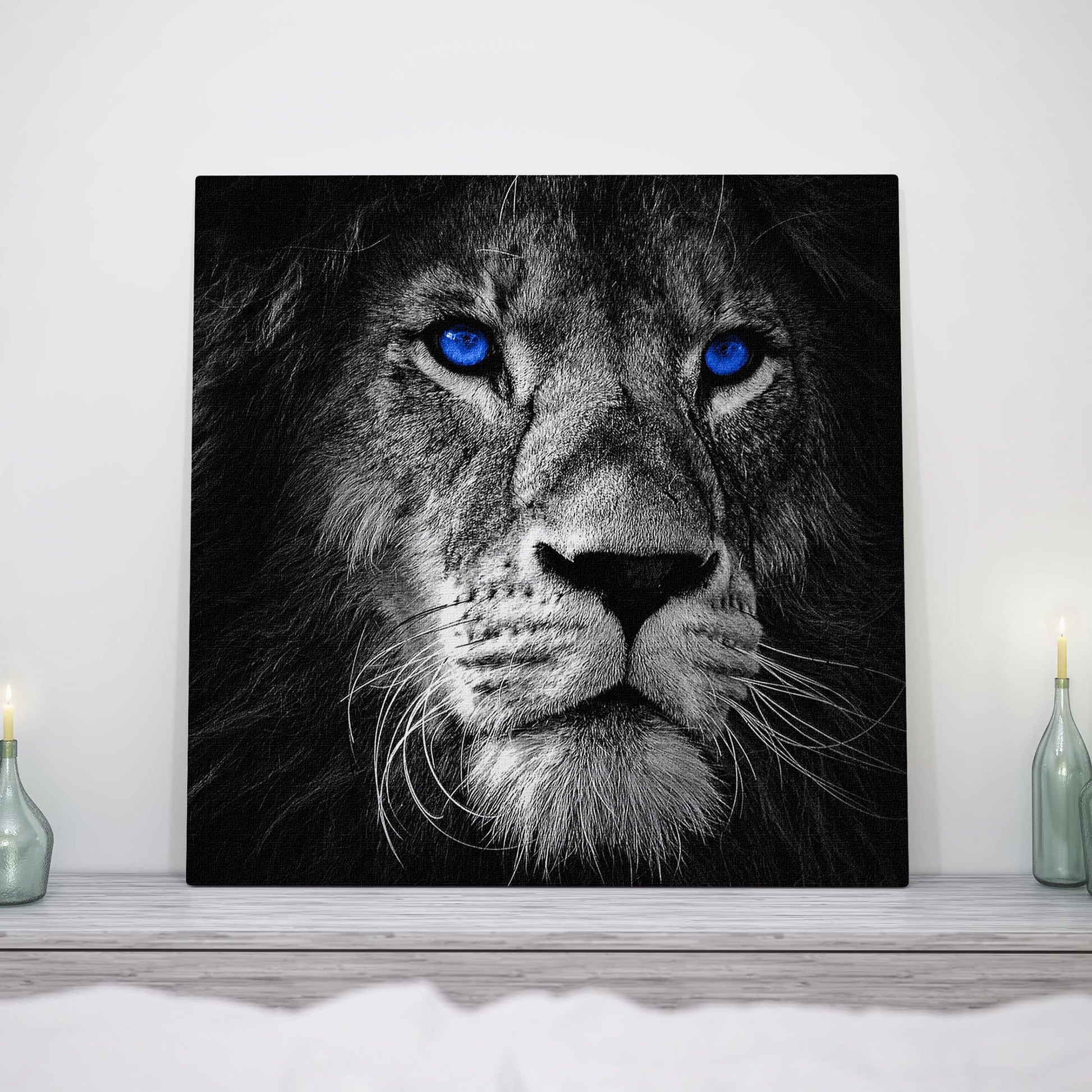 Black and white close-up lion face with vivid blue eyes printed on square canvas displayed on white mantelpiece between candles