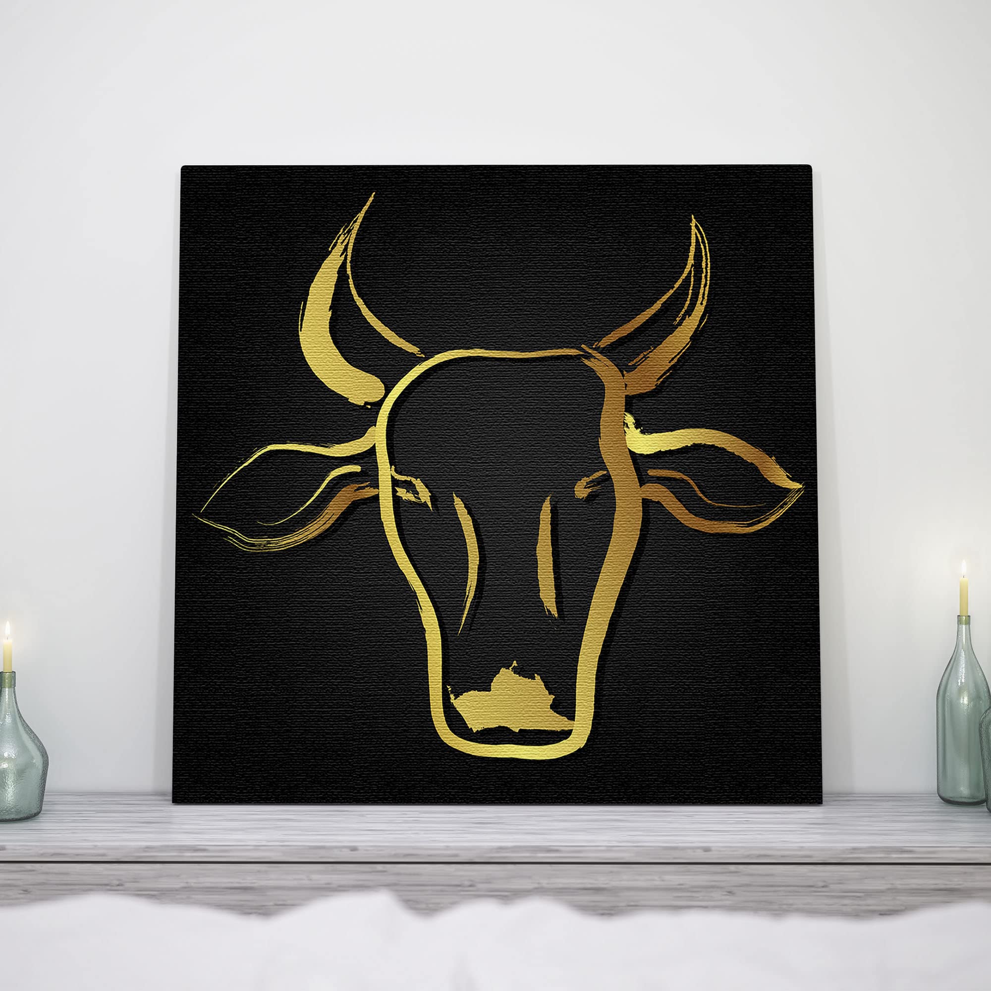 Black and gold abstract cow head art with sleek brushstroke design on square canvas displayed on white shelf with candles