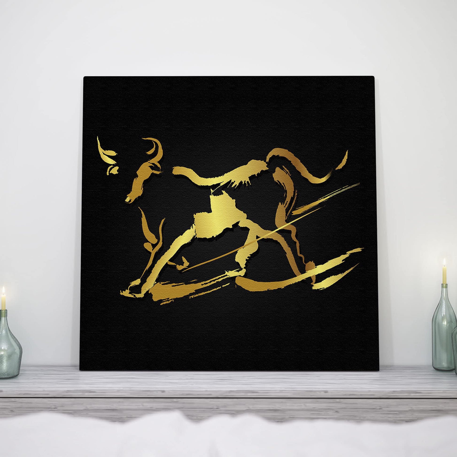 Abstract black and gold bull wall art with bold brushstroke design on square canvas displayed above minimalist mantel with candles